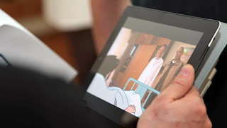 Auf dem Bildschirm eines Tablets ist eine Arztvisite am Krankenbett zu sehen