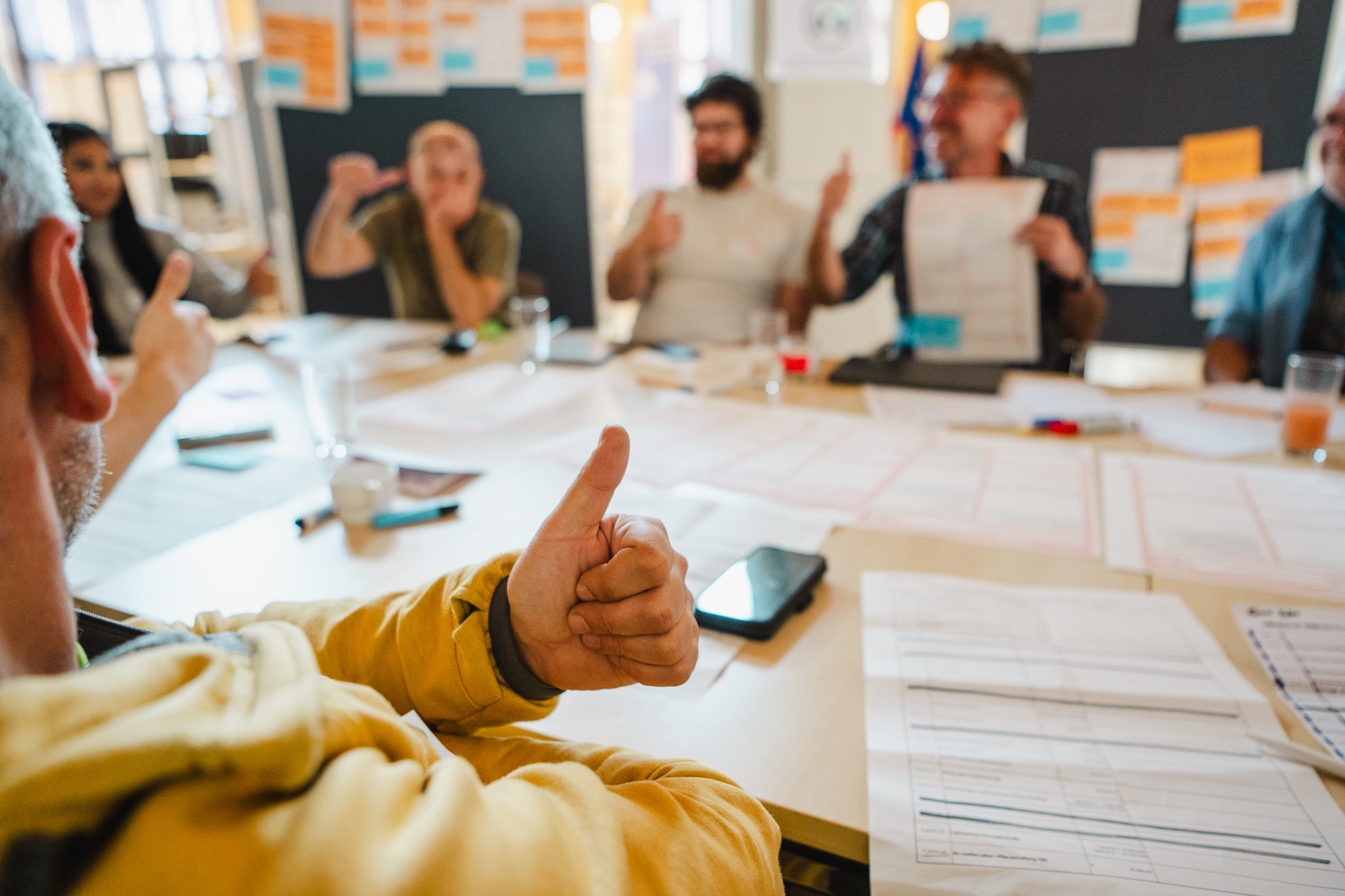 Teilnehmende eines Workshops sitzen an einem Tisch und zeigen Daumen nach oben